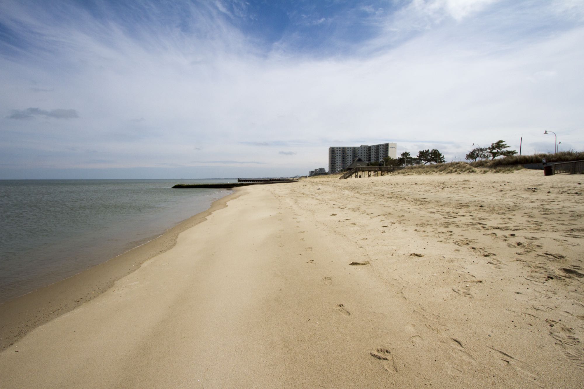 The narrow Bay-front beach along Willoughby Spit, Norfolk, with a jetty and condo tower in the distance